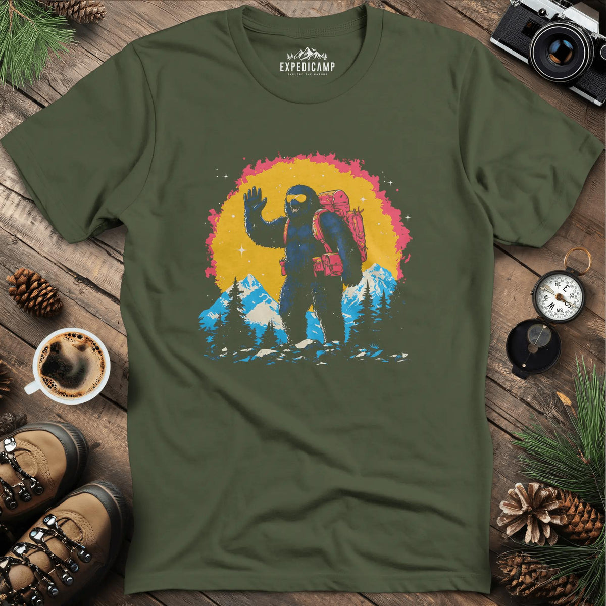 Bigfoot Waving T-Shirt – Friendly Sasquatch in the Mountains – Military Green – Outdoor apparel for travel, hiking, camping, and nature lovers – ExpediCamp
