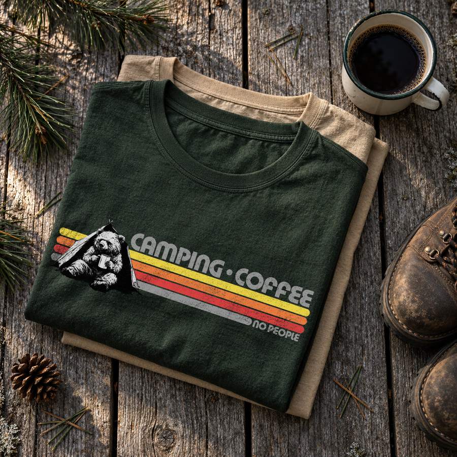 Folded ExpediCamp t-shirts on a wooden table with a coffee mug and hiking boots